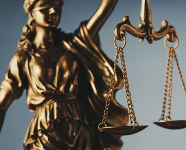 Figure of Justitia or Justice holding the scales of justice with close up focus to the scales symbolic of the law over grey